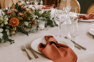 Mesa de casamento com toalha off-white, folhagens verdes e detalhes terracota